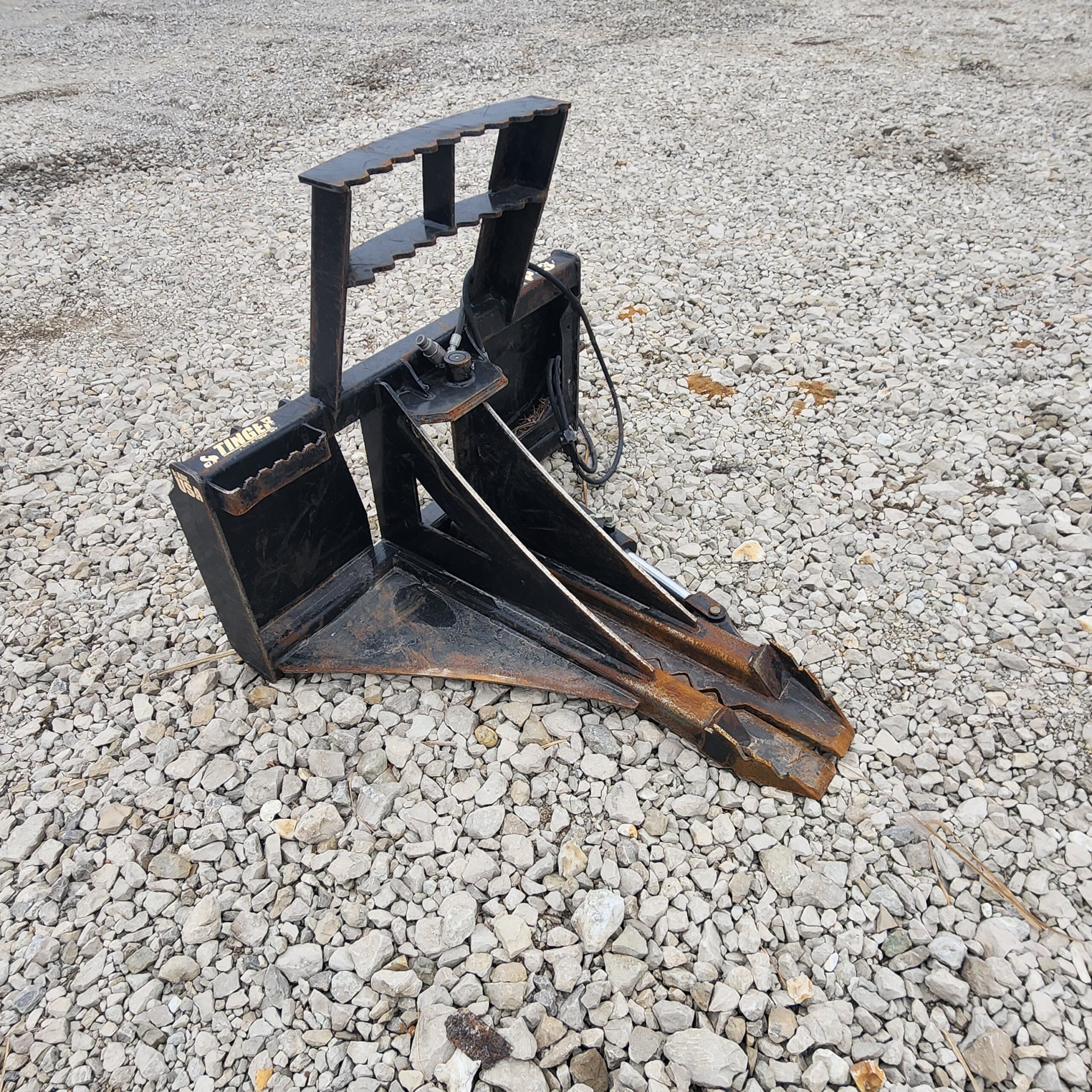 Black metal construction attachment with serrated edges rests on gray gravel.