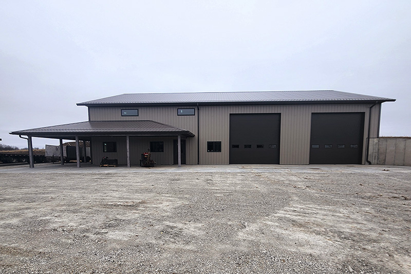 A large, gray metal warehouse with two big garage doors and a smaller covered entrance used to store RV's . Offered for rent by Cornerstone Equipment Rental.
